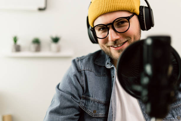 istock Young smiling man recording podcast and doing live streaming using microphone and headphones in recording studio 1487492761