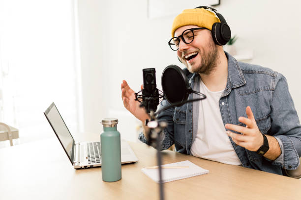 istock Young smiling man recording podcast and doing live streaming using microphone and headphones in recording studio 1487492804