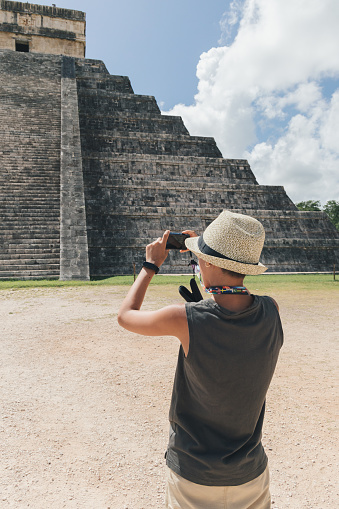 Teenage girl with hat taking a picture of the pyramid of Kukulcan in Chichen Itzá, Mexico