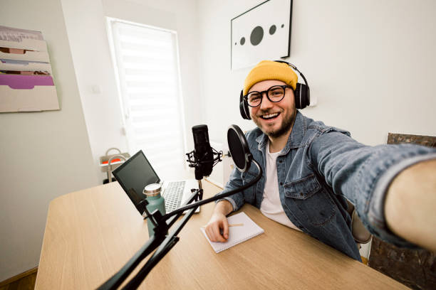 istock Self portrait of Young smiling man recording podcast and doing live streaming using microphone and headphones in recording studio 1487493648