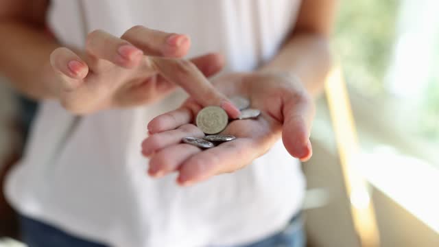 Poor female person stands counting small coins on palm