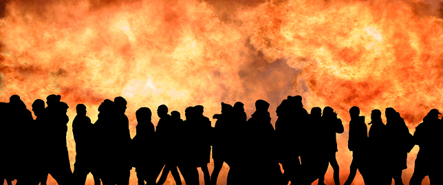 Image of black silhouettes of many people against the background of a solid wall of fire