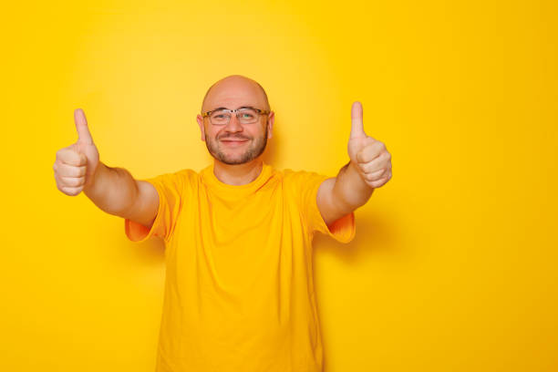 istock Mid 30s bald man showing thumbs up on yellow colored background 1487495538