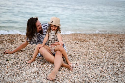 Mom and daughter with straw hat's sitting on the sand. family playing at seaside.