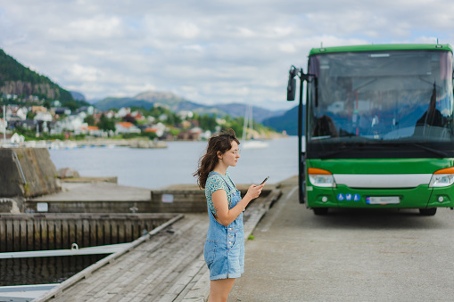 Young Caucasian woman waiting for the bus and using app on smartphone to check the schedule