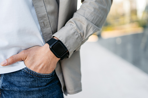 Handsome young man wearing a smart watch in front of a corporate building outdoors. Close-up.