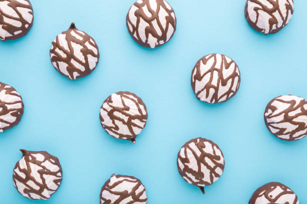 Pink soft zephyr covered with dark brown chocolate glaze on light blue table background. Pastel color. Closeup. Sweet snack. Food pattern. Top down view.