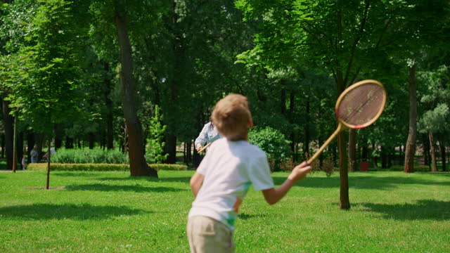 Joyful mother play badminton with son in park. Happy family have fun outdoor.