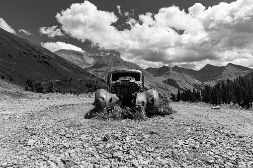A greyscale shot of an aged pickup truck in front of a mountain range, San Juan