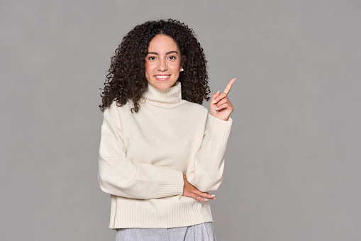 Young happy latin professional business woman pointing finger aside isolated on light brown background. Smiling female model showing advertising business commercial service ads concept.