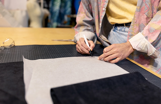 Close-up of a fashion designer making a paper pattern for creating new dress design at creative studio. Fashion stylist working on creating new dress designs inside makers space.