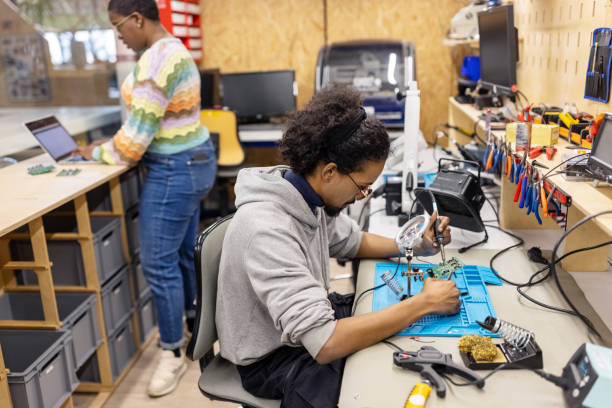 istock Man working on circuit boards at desk with a woman working on laptop at makers space 1487508024