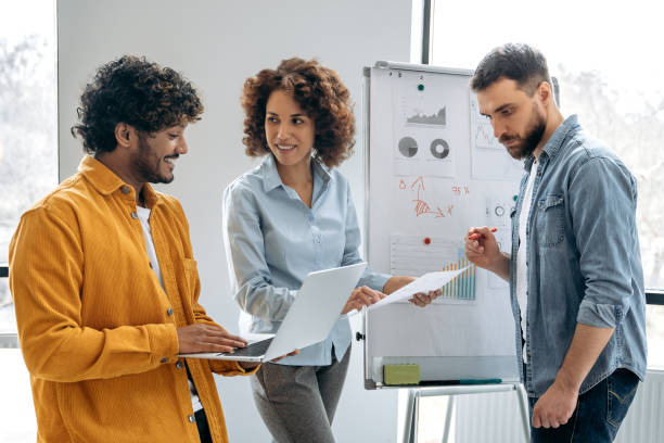 istock Teamwork concept. Positive busy successful multiracial colleagues, office employees, managers, stand in a modern office near the marker board, analyze and discuss financial charts, profit, risks 1487508320