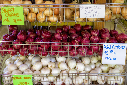 A variety of onions for sale in wire baskets at an open-air Market.