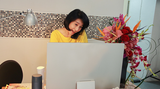 An Asian female flower art teacher, the owner of a small business flower art classroom, watches the registration status of students on the computer and communicates with the students. The day-to-day life of running a small business with technology