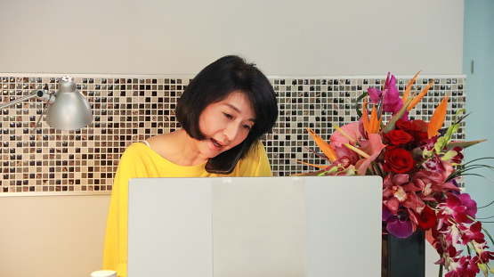 An Asian female flower art teacher, the owner of a small business flower art classroom, watches the registration status of students on the computer and communicates with the students. The day-to-day life of running a small business with technology