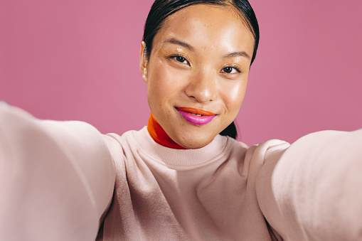 Female looking at the camera while taking a selfie in a studio, she is wearing a bold two tone lipstick. Woman in her 20’s enjoying her new makeup look in a studio.