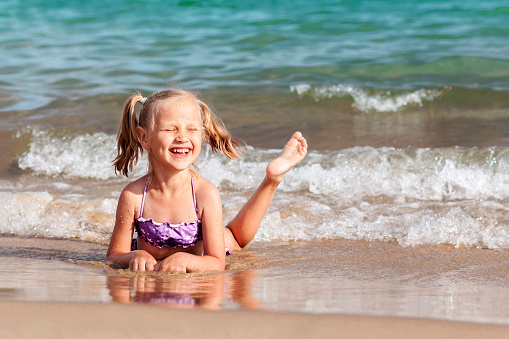 Cute little girl is laying by the water and playing with sand on the beach