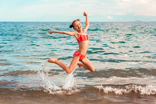 Having fun on Sea Coast. Happy Child Little Girl Kid in Swim Jumping on Sunny Beach. Happy Summer Holiday.