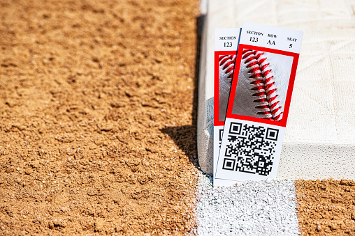 A low angle view of a pair of baseball game ticket stubs next to third base in the infield of a baseball diamond.