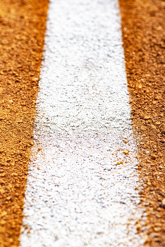 A close-up of a painted white Fair-Foul Line on dirt of a baseball/softball  infield diamond. Sometimes this can be referred to as a Fair Line as it is in Fair Territory and the area from the edge of the line is Foul Territory.