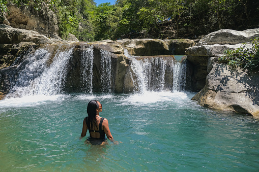 Close up rear view shot of Asian woman standing inside a natural waterfall plunge pool in Sumba island