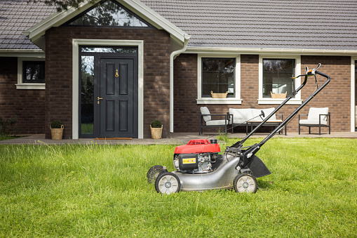 Mature man pushing a lawnmower round a lawn in front of cottage.