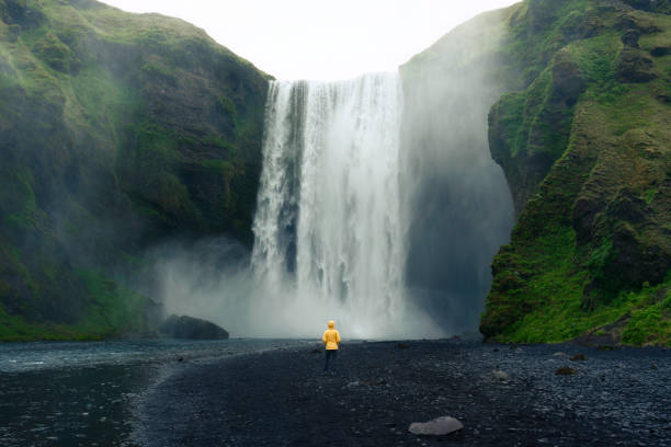 Skogafoss waterfall flowing with asian woman standing in summer at Iceland Dramatic scenery of Skogafoss waterfall flowing with asian woman standing in summer at Iceland iceland stock pictures, royalty-free photos & images