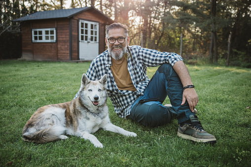 Mature men playing with his dog at backyard of cottage.
