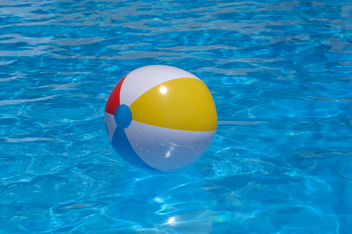 Colorful inflatable beach ball floating in swimming pool on background of blue water. Family summer vacation, holiday and kids pool party. Healthy outdoors sport activity
