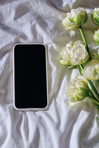 Close-up smartphone on the bed next to a bouquet of flowers. Copy space for text and information to your phone. Focus on your phone screen. Surprise gift