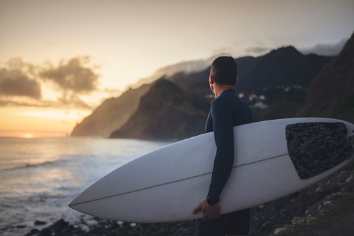 Surfer with his board on the beautiful shore of the ocean at sunrise.