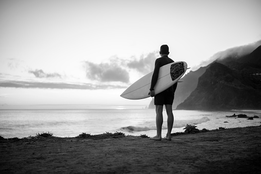 Black and white photo of a Caucasian man who is at the beach in Hawaii with his family, playfully throwing his Eurasian toddler son up into the air while his wife swims nearby and watches.