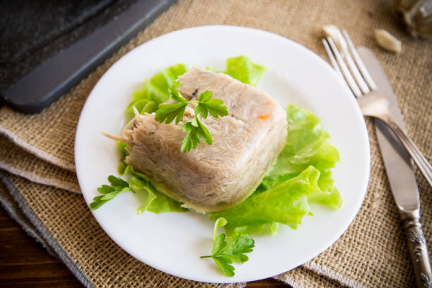 Boiled chicken meat aspic in meat gelatin broth in a plate on a wooden table