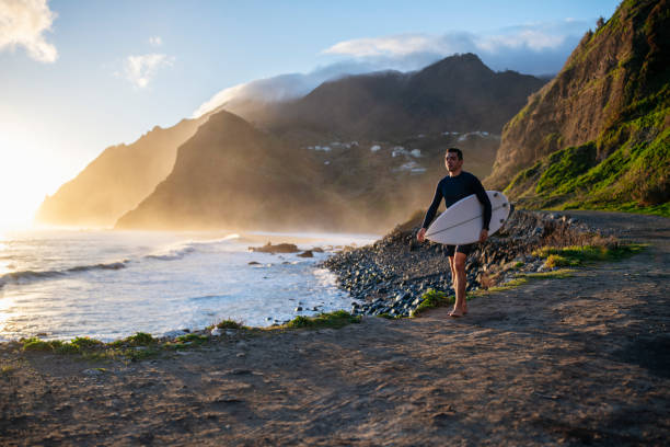Surfer walking on a beautiful beach at sunrise.