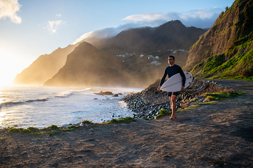 Handsome middle aged surfer walking on a beautiful beach by the ocean at sunrise.