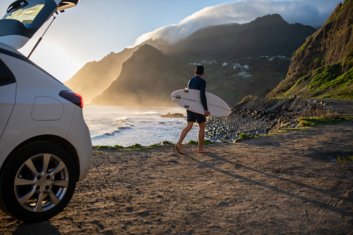 Rear view of a middle aged surfer looks out towards the beach.