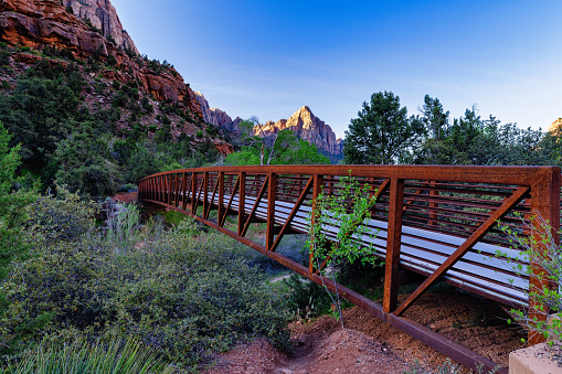 The Watchman Scenic View Along the Virgin River - Zion National Park iconic view in springtime of red rock formation with bridge and recreation path.