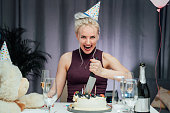 Attractive crazy laughing birthday woman with bread-knife planning to cut her birthday cake while celebrating birthday at home alone. Selective focus