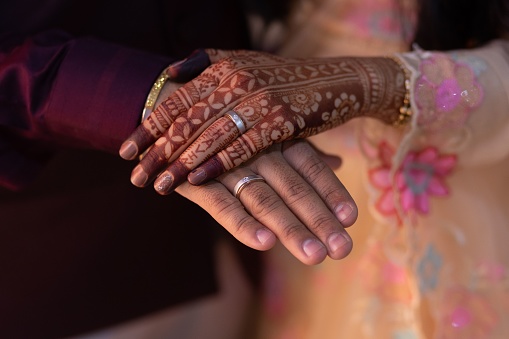 A happy wedding couple holding hands. The woman's hand with intricate henna.