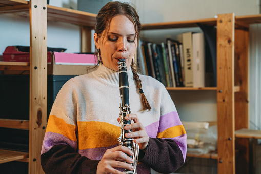A woman is playing clarinet for practice. She's in a studio at home.
