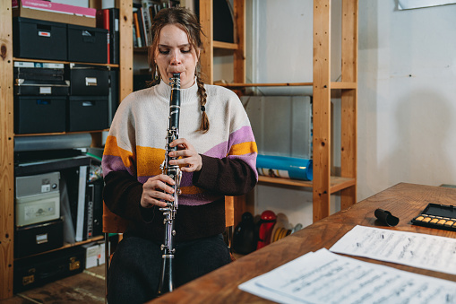 A woman is playing clarinet for practice. She's in a studio at home.