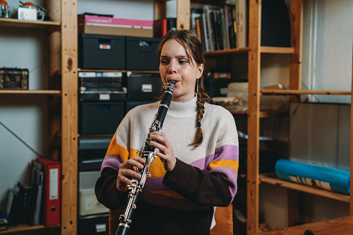 A woman is playing clarinet for practice. She's in a studio at home.