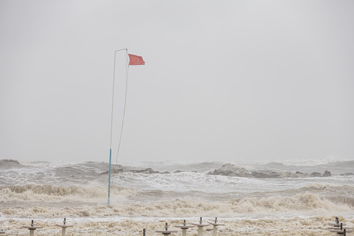 Wide angle view of a beach in popular Adriatic coast with raging sea and waves eating up the sand. Red flag waving, danger keep out of the water.