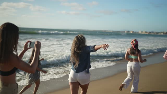 Female friends having fun and filming while walking on the beach