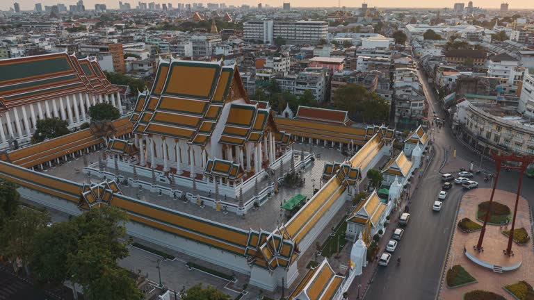 Aerial hyper lapse drone point of view over Wat Suthat Thepwararam(Suthat Thepwararam temple) and Giant Swing (Sao Chingcha) Bangkok Thailand, A popular famous tourist travel landmark with vehicle and traveler commuting along street at twilight time.