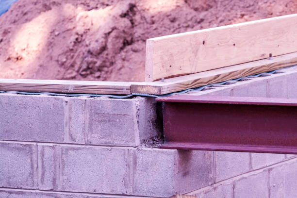 Detail at a residential home addition in-law apartment new build construction project. A steel i-beam girder which will eventually support the first level sub-floor has been lowered into position in a notch cut into a corner of the basement concrete block masonry.