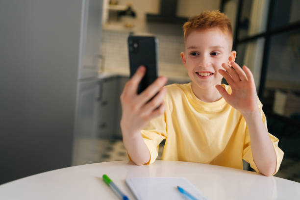 cheerful child school boy holding phone distance learning class using mobile application, watching online lesson, video calling in app making notes - homework teenager mobile phone school imagens e fotografias de stock