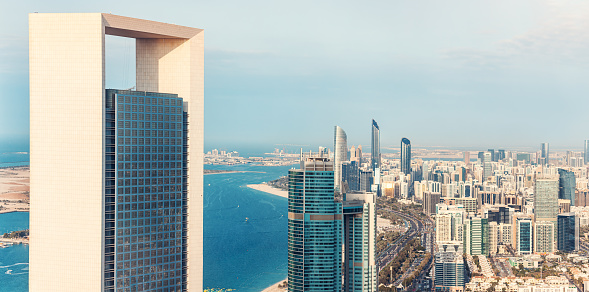 A breathtaking view of Abu Dhabi's iconic skyscrapers rising majestically from the ground, their gleaming glass facades reflecting the bright blue sky above.