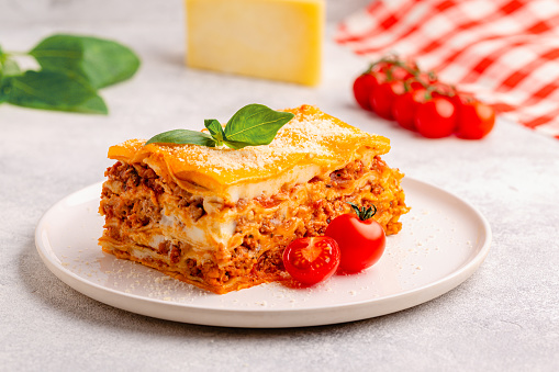 Traditional lasagna with bolognese sauce topped with basil leaves served on a white plate